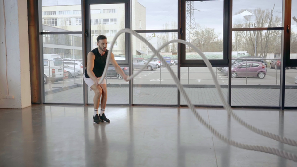 Bearded sportsman in white shorts doing exercise with ropes in gym - Video