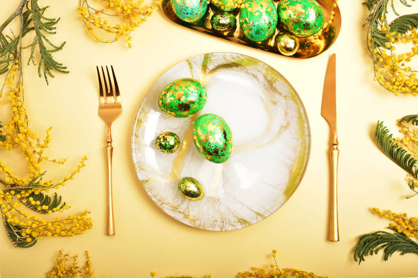 Table setting in easter style. Mimosa, painted green eggs, golden cutlery. - 写真・画像