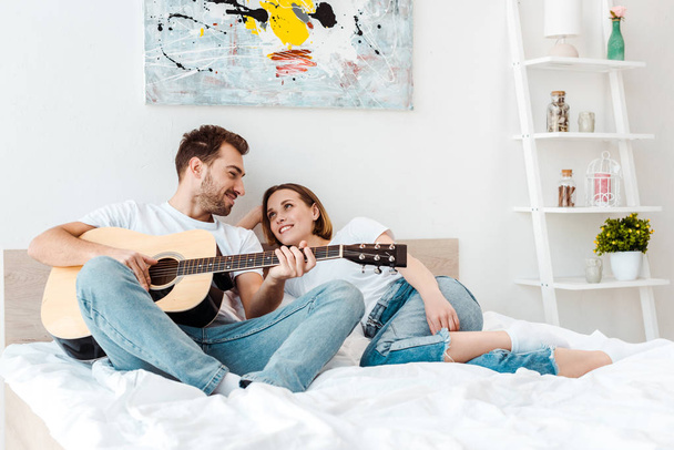Homme souriant couché sur le lit avec sa femme et jouant de la guitare
 - Photo, image