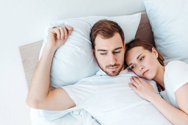 задумчивая пара в белых футболках лежит на кровати и смотрит в сторону
 - Фото, изображение