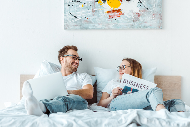 couple in glasses with laptop and newspaper looking at each other - Фото, зображення