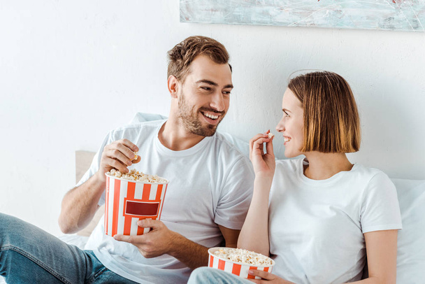 Örömteli mosoly pár evés Popcorn az ágyban, és nézi egymást - Fotó, kép