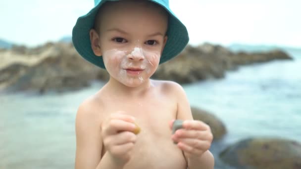 Aranyos fiú Sunblock krémmel egy szalmakalapot a strandon - Felvétel, videó