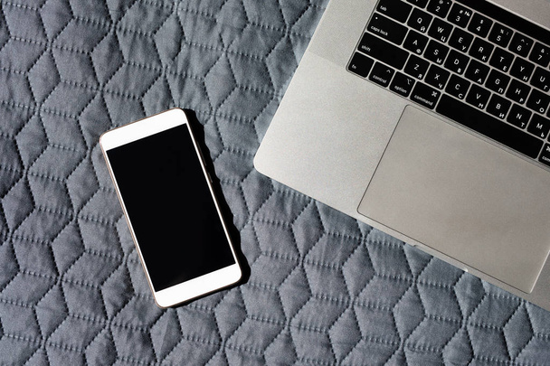 Blank smartphone screen near laptop keyboard on the bed - Zdjęcie, obraz