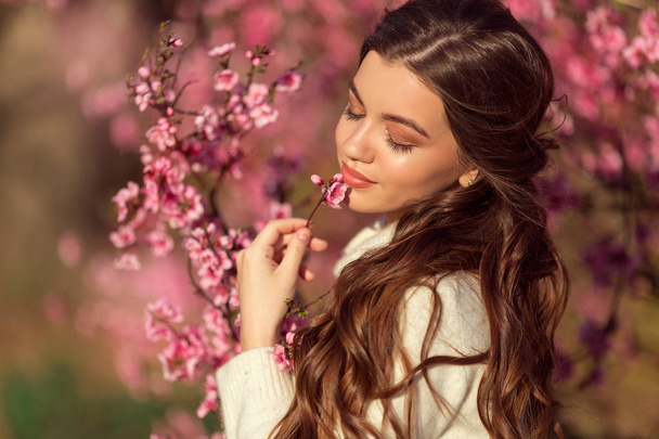 Porträt eines jungen schönen Mädchens, das in der Nähe eines Blütenbaums mit rosa Blumen posiert. - Foto, Bild