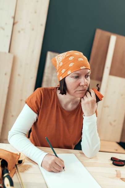 Female carpenter is drinking coffee and planning DIY project - Фото, изображение