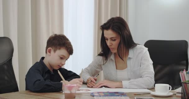 gut aussehende erwachsene Mutter, die eine Zeit mit ihrem Sohn verbringt, malen sie gemeinsam am Leben in einem modernen Hausdesign - Filmmaterial, Video