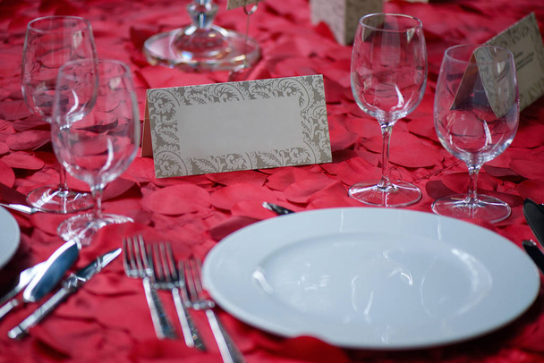Fine dining table setting with white china and wine and water crystal glasses, with silverware in the order of use, and romantic red tablecloth ready for guests at an event, wedding or at a restaurant - Photo, Image