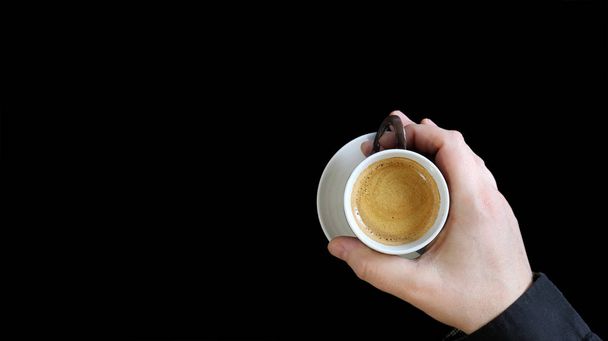 Male hand holding a coffee cup. Close up of a hand of man holding a warm mug with fresh coffee isolated on black background. Coffee concept - Photo, Image