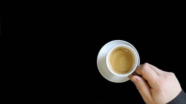 Male hand holding a coffee cup. Close up of a hand of man holding a warm mug with fresh coffee isolated on black background. Coffee concept - Photo, Image