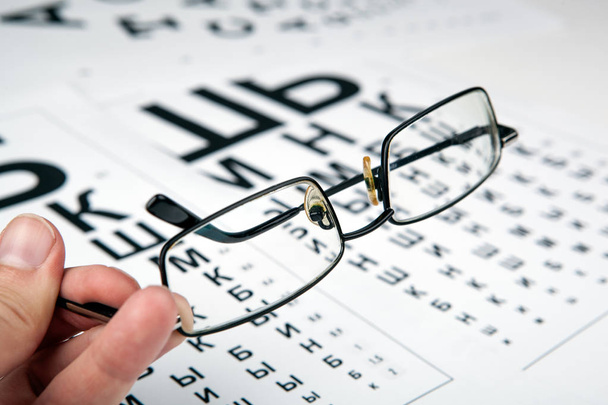 Brille auf dem Tisch mit Schrift zur Bestimmung der Sehkraft - Foto, Bild