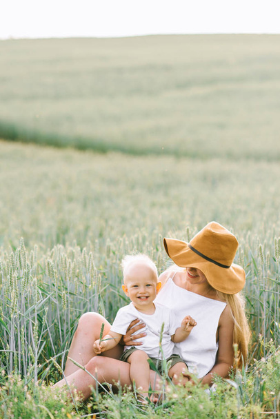 a young mother and her little child sitting near the wheat on a  - Foto, afbeelding
