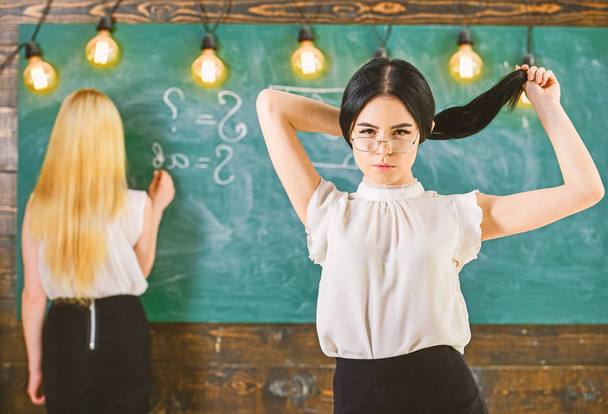 Students and trainees concept. Attractive women preparing for lesson. Student, teacher in eyeglasses stand in classroom. Girl looks attractive while lady writing on chalkboard background, defocuse - Photo, Image