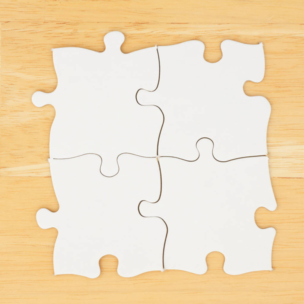 Cuatro piezas de rompecabezas en blanco sobre fondo de madera de escritorio texturizado
 - Foto, imagen