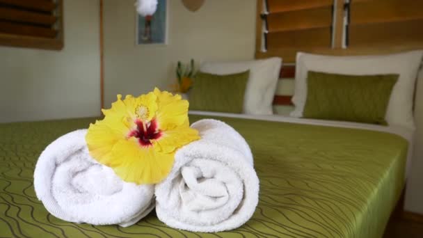 CERRAR UP Flor de hibisco amarillo revoloteando sobre toallas enrolladas en un dormitorio de hotel cuidadosamente decorado. Acogedor bungalow romántico en un resort tropical. Tranquilo escondite para relajarse de vacaciones
 - Metraje, vídeo