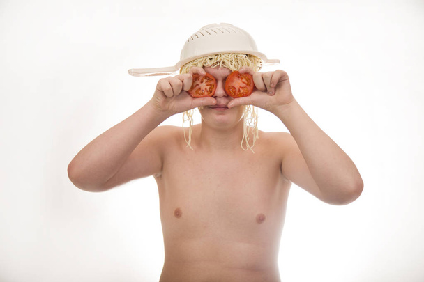 Un chico joven, gordo, alegre, sonriente, con tomates y un colador y fideos de espagueti en la cabeza. Cuerpo regordete sin ropa. Fondo blanco. Foto de retrato
. - Foto, imagen
