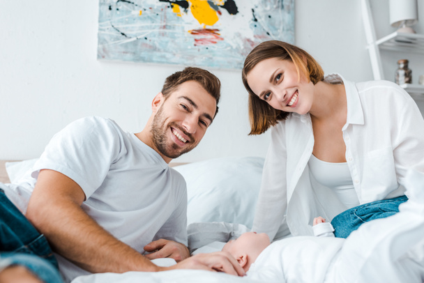 smiling young parents with baby looking at camera in bedroom - Foto, Imagen