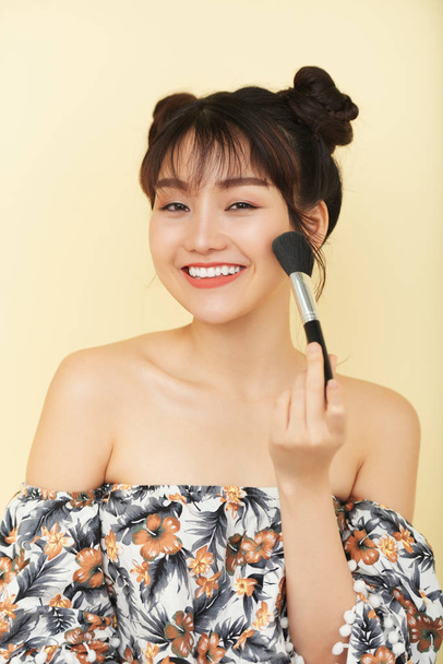 Joyful young Asian woman with cute two buns applying bronzer - Zdjęcie, obraz