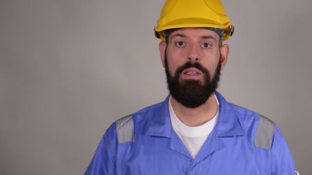 Portrait of young worker in yellow helmet explain something and show ok gesture on gray background - Imágenes, Vídeo