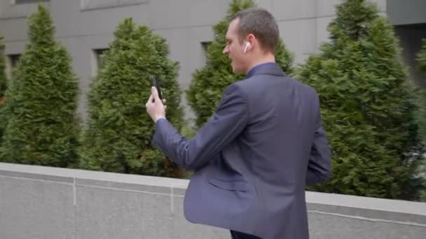 Giovane uomo d'affari cammina con auricolari wireless e conduce aggressivamente una discussione su una videochiamata su smartphone. Un ragazzo con un bicchiere di caffè in mano mostra il suo dispiacere in una videoconferenza
 - Filmati, video