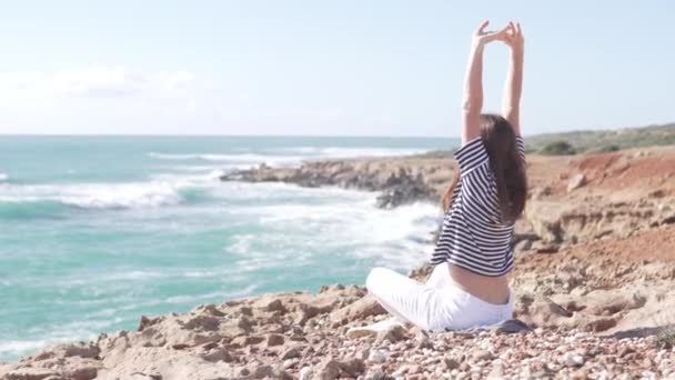 Młoda kobieta siedzi na skale nad oceanem - Materiał filmowy, wideo