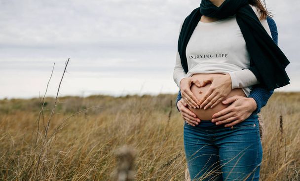 Schwangere macht Herz mit Händen auf nacktem Bauch mit Partner - Foto, Bild