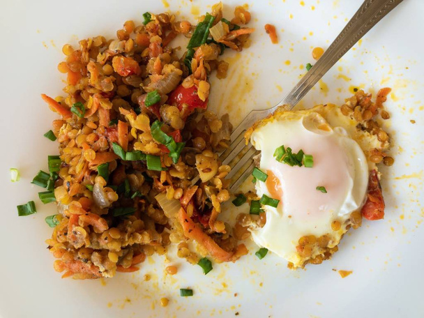 Вид сверху на тарелку с жареным яйцом, красная чечевица с овощами и вилкой
 - Фото, изображение