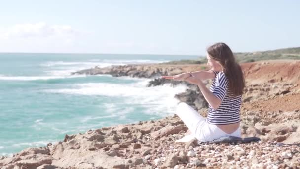 Τουρίστας σε ένα όμορφο μέρος σε ένα βράχο δίπλα στη θάλασσα κάνοντας γυμναστική - Πλάνα, βίντεο