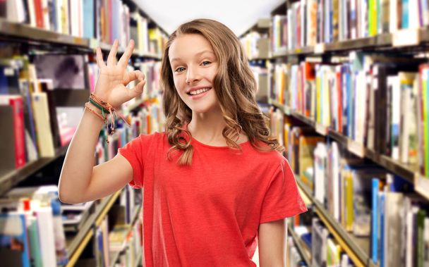 smiling teenage student girl showing ok at library - Фото, изображение