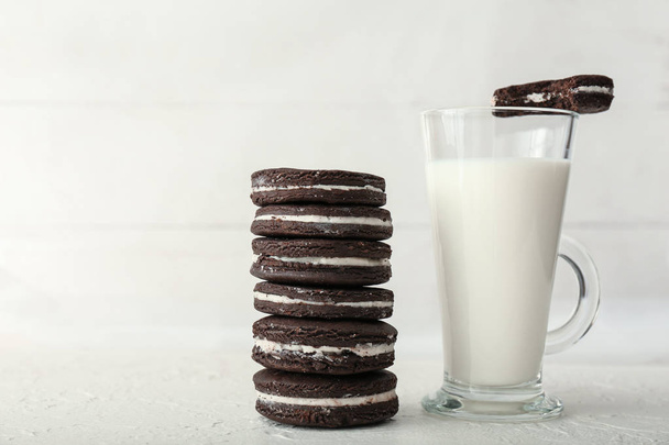 Pilha de biscoitos de chocolate saborosos com copo de vidro de leite no fundo leve
 - Foto, Imagem