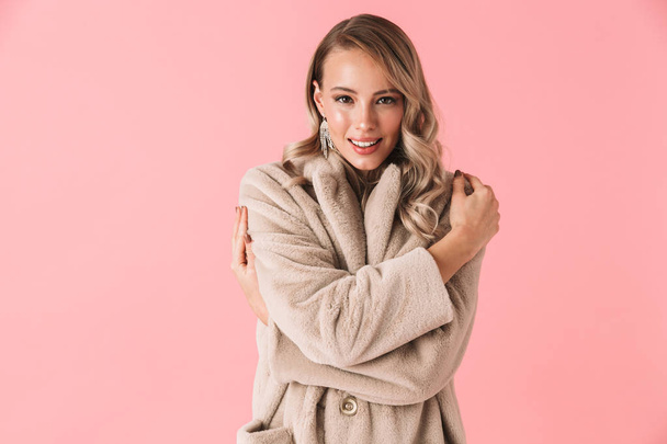 Pretty woman posing isolated over pink wall background dressed in fashion coat. - 写真・画像