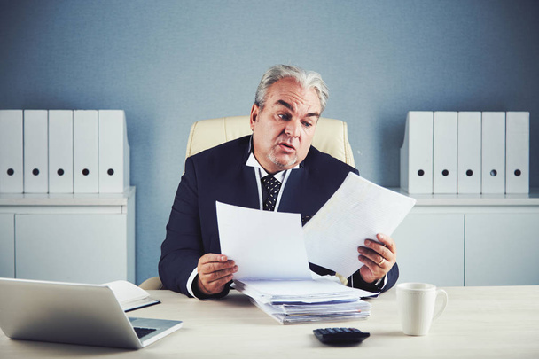 Серьезный зрелый предприниматель, работающий с финансовыми документами
  - Фото, изображение