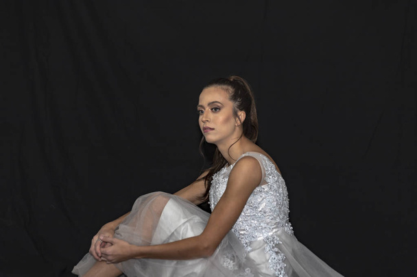 Portrait of a girl with long hair and green eyes in a wedding dress sitting on the floor. Black background - Foto, Bild