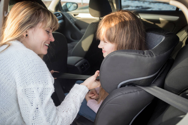 ママは子供の車の座席でベルトを固定するために彼女の娘を助ける - 写真・画像