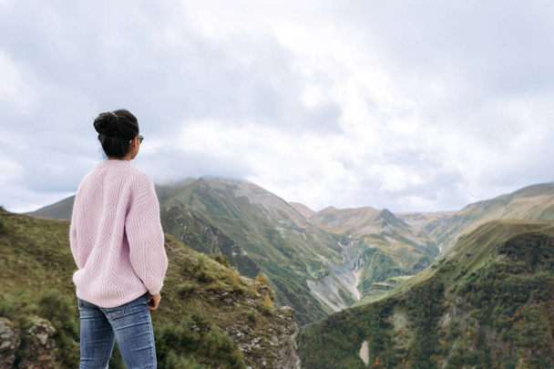 young girl in a sweater is looking at the Caucasian mountains - Photo, image