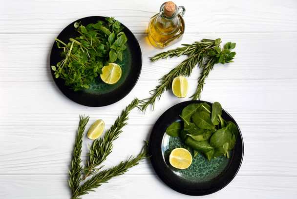 Layout of vegetarian products on two plates with spinach and basil, a bottle of olive oil, rosemary branches, lime on a light wooden background. - Photo, Image