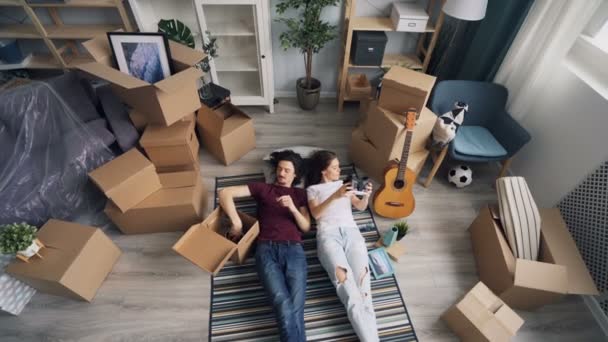 Happy couple taking things from box lying on carpet relaxing during relocation - Video