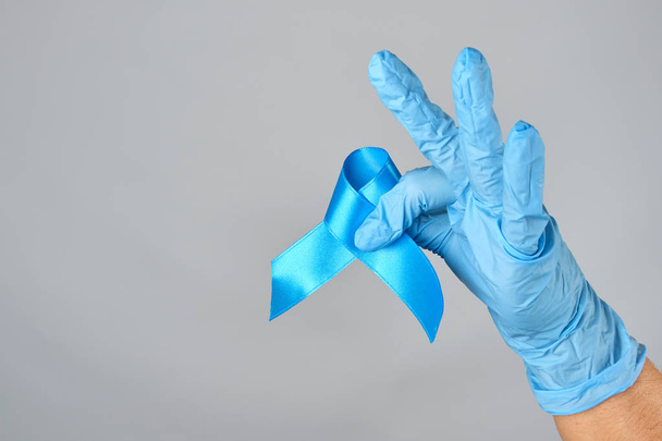 hand in blauwe latex handschoen met een blauw lint - Foto, afbeelding