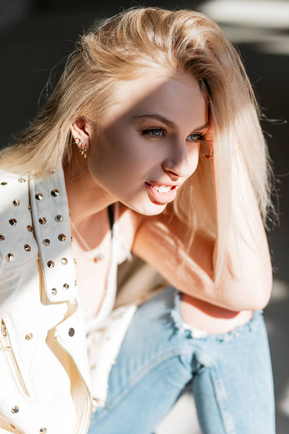 Porträt einer glücklichen hübschen jungen Frau mit schönen blauen Augen mit blonden Haaren und prallen sexy Lippen in einer ledernen, modischen Frühlingsjacke an einem sonnigen Tag. niedliches Mädchen Modell genießt helles Sonnenlicht. - Foto, Bild