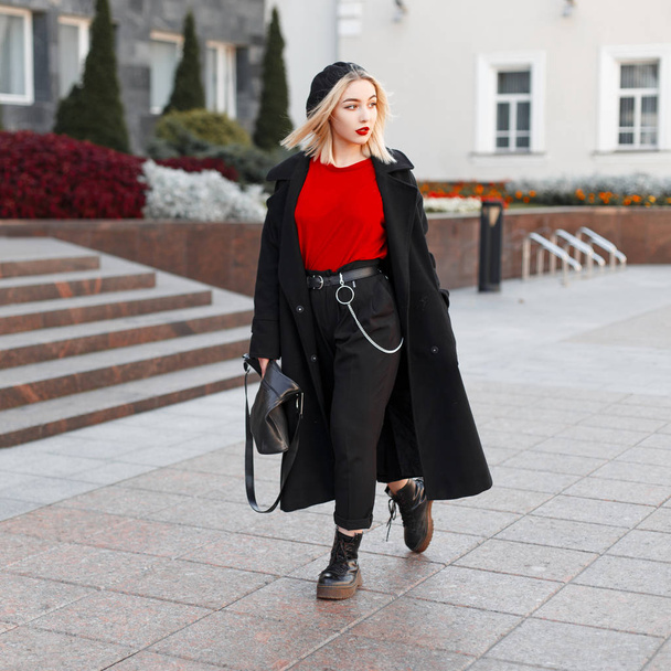 Young beautiful woman with blond hair with a leather handbag in a black autumn fashionable outerwear in a stylish beret walks around the city on a warm autumn day. Pretty girl on vacation.Modern style - Photo, Image