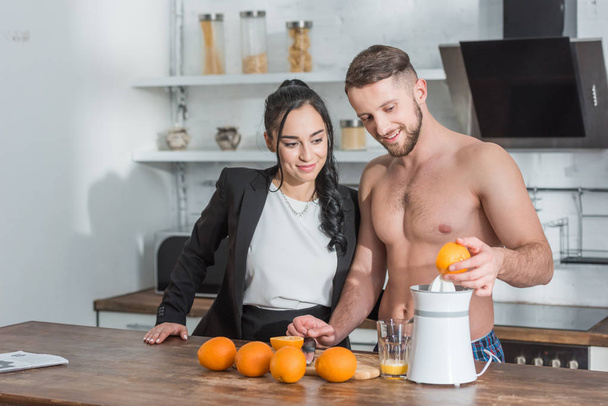 homem sem camisa alegre preparando suco de laranja perto de menina atraente
  - Foto, Imagem