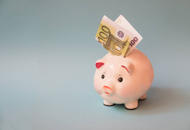 Piggy bank with euro banknote inserted in slot, on blue background. Financial planning, savings and investment concept. - Photo, image