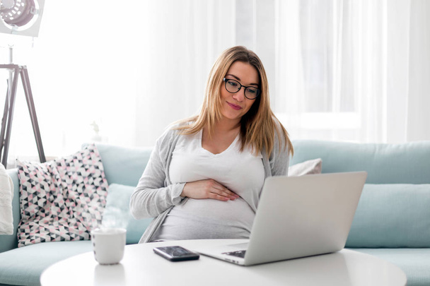 Femme enceinte travaillant en ligne avec ordinateur portable à la maison, concept freelance
 - Photo, image