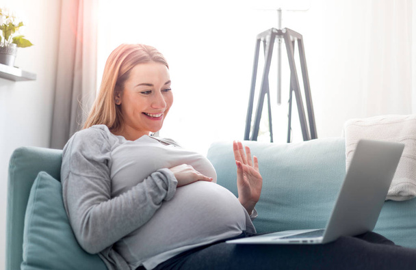 Pregnant woman video chatting with family on laptop waving hand to screen - Zdjęcie, obraz