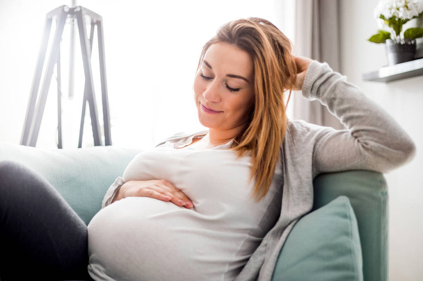 Pregnant woman relaxing at home on the couch - Foto, Bild