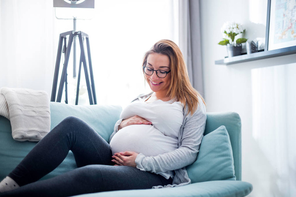 Pregnant woman relaxing at home on the couch - 写真・画像