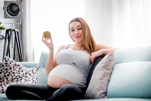 Nutrition and Diet during pregnancy, Pregnant woman eating fruits sitting on sofa at home - Fotoğraf, Görsel