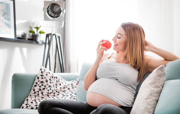 Nutrition and Diet during pregnancy, Pregnant woman eating fruits sitting on sofa at home - Φωτογραφία, εικόνα