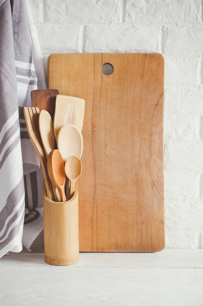 Drewniane lub bambusowe sztućce, ręcznik i deska do krojenia we wnętrzu białej kuchni. - Zdjęcie, obraz