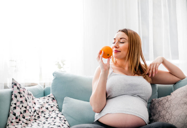 Nutrition and Diet during pregnancy, Pregnant woman eating fruits sitting on sofa at home - Fotografie, Obrázek